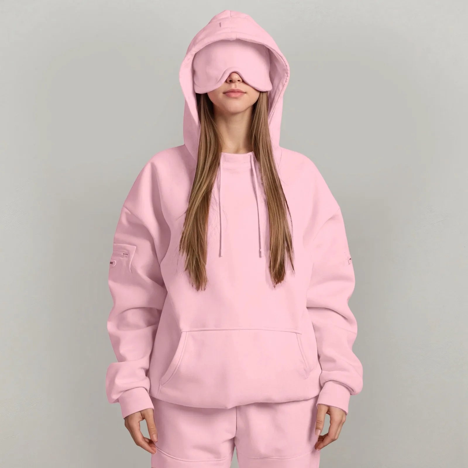 Person wearing a pink hoodie and matching pants with a matching sleep mask on a gray background